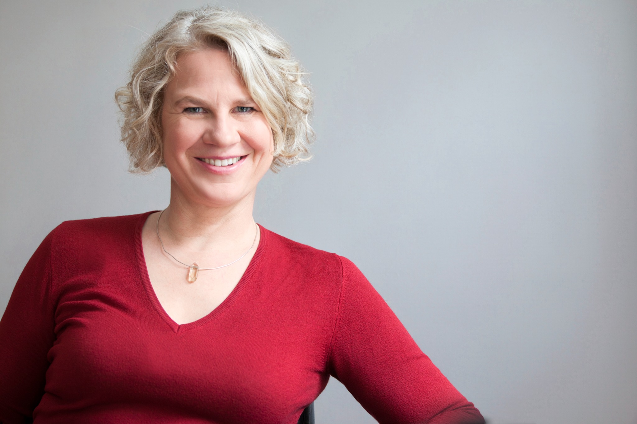 Dr. Yvonne Konstanze Behnke im roten Oberteil vor dem originalen hellgrauen Hintergrund.