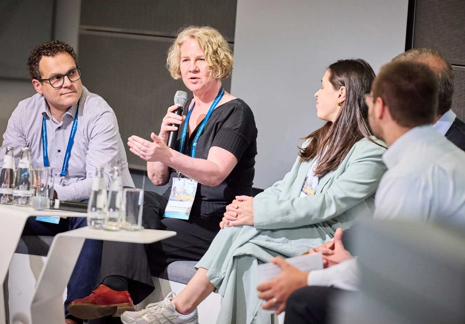 Yvonne Behnke spricht und gestikuliert mit Mikrofon im Fraunhofer-FOKUS-Panel; weitere Panelgäste sind sichtbar.